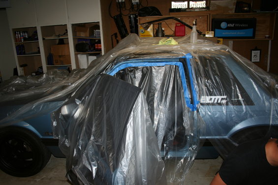 Light blue Ford Mustang covered in plastic, doors taped off