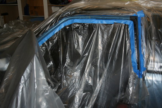 Car door frame covered in plastic sheeting with blue painter's tape