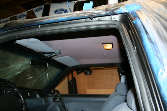 Interior of a Ford Mustang, possibly from the late 80s or early 90s, with sun visors up and plastic sheeting covering parts of the exterior