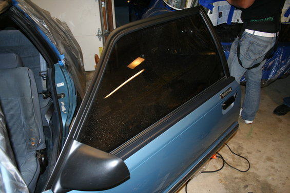 Blue 1990 Ford Mustang door open, showing interior and exterior. Tinted window reflects light