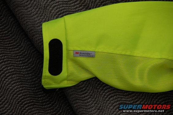Neon yellow jacket sleeve with 3M Scotchlite reflective material tag and black velcro patch on textured gray background