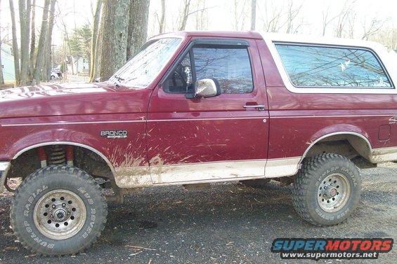 Maroon Ford Bronco with a white top, side view. Mud on the lower body