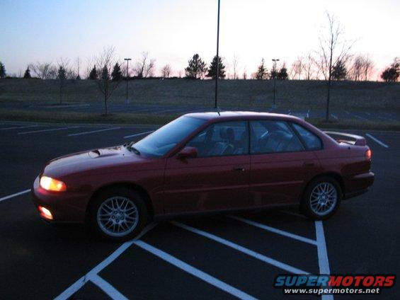 Red 1997 Subaru Legacy sedan parked in a lot at dusk, side view