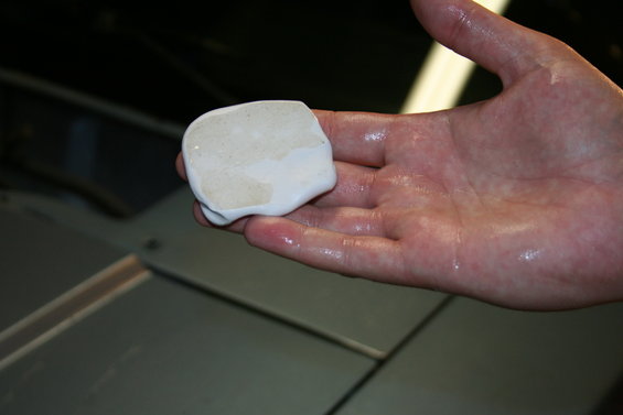 Hand holding a piece of white detailing clay over a car's hood