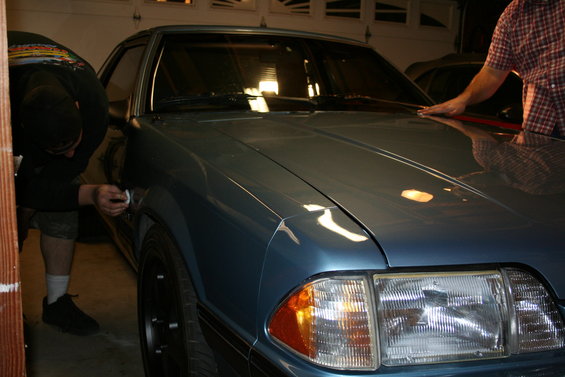 Blue coupe with black wheels, being worked on in a garage