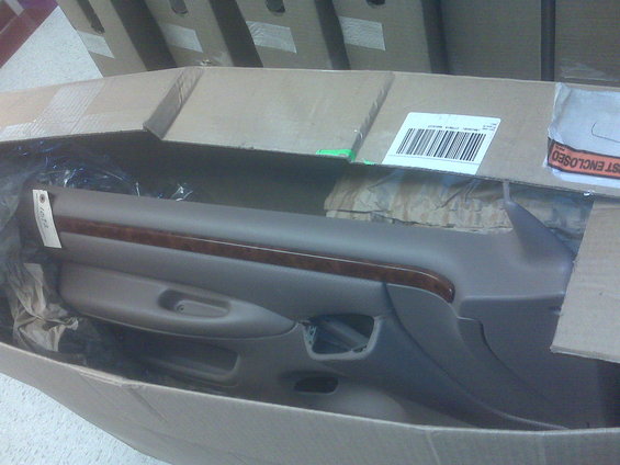 Car door panel with wood trim, wrapped in plastic inside a cardboard box