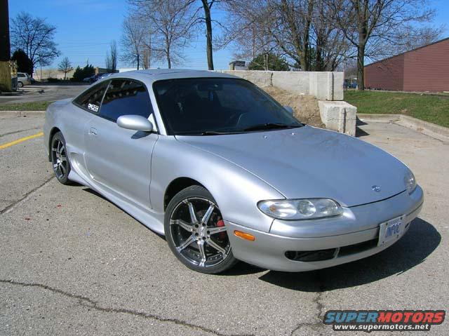 Silver 1994 Mazda MX-6 coupe with aftermarket wheels parked on asphalt