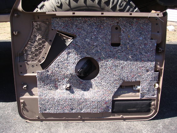 Tan car door panel with insulation and speaker hole. Tire tread visible at top