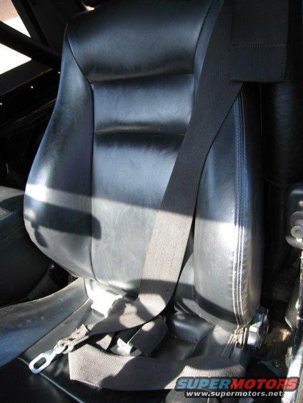 Black leather bucket seat with a black seatbelt. Some text is visible at the bottom right