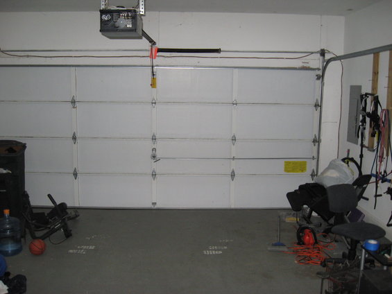Garage with a closed white sectional door, a trash can, a basketball, and some equipment