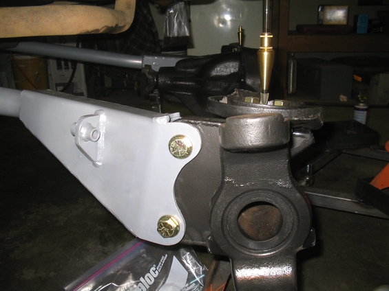 Close-up of a vehicle's suspension components, possibly a steering knuckle and control arm, with new gray paint and gold bolts