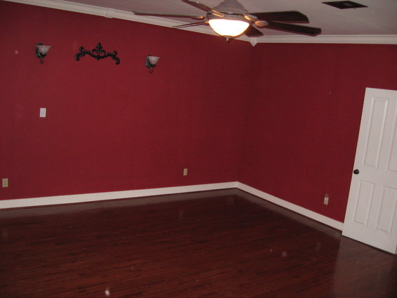 Interior scene with red walls, dark wood floor, ceiling fan, and white door