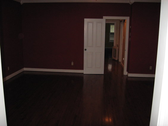 Interior of a room with dark wood floors, maroon walls, and a white door ajar leading to a hallway