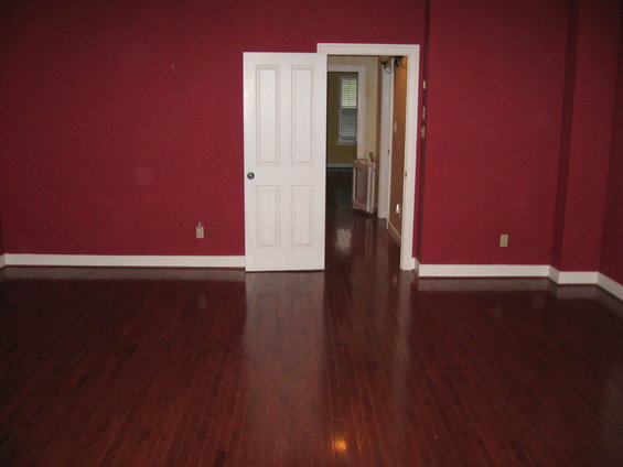 Interior of a room with dark red walls and a polished wood floor. An open white door leads to another room with a window