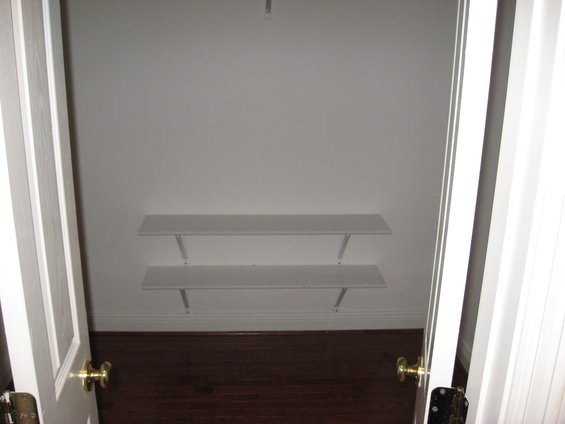 Empty closet interior with two white shelves and dark wood floor