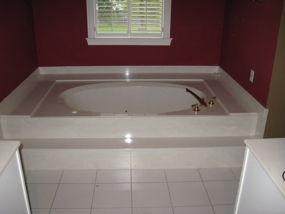 Bathroom with a large built-in bathtub, brass fixtures, and a window with white shutters