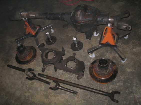 Axle assembly on jack stands with brake rotors, hubs, and drive shafts on concrete floor