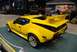1996 Ford Bronco - A bright yellow sports car is displayed indoors, with a Jeep and vendor tents in the background.