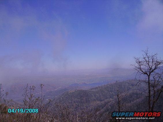 Misty mountain landscape with bare trees in the foreground and a blue sky