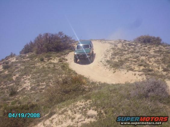 Green 1990 Ford Bronco driving up a dirt hill