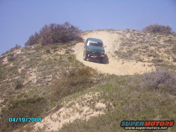 Green 1990 Ford Bronco driving up a sandy hill