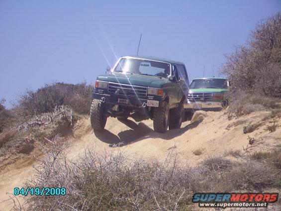 Green Ford Bronco on a dirt hill, front wheel lifted