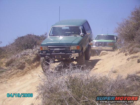 Green 1990 Ford Bronco on a dirt trail with another Bronco behind it