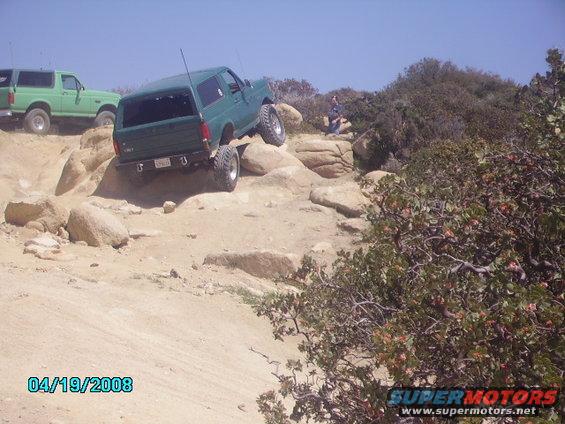 Green Ford Bronco climbing rocks, lifted suspension, off-road tires, another green Bronco behind it