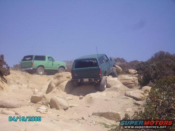 Rear view of a 1990 Ford Bronco navigating rocks, with another Bronco behind