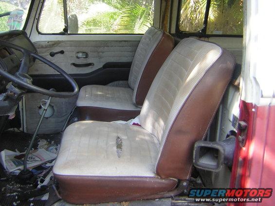 Interior view of a van showing two worn seats, dashboard, and steering wheel. Torn upholstery on the driver's seat