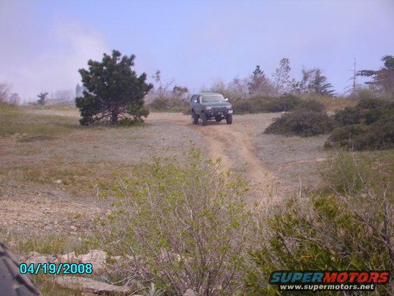 Green 1990 Ford Bronco driving on a dirt road, front view