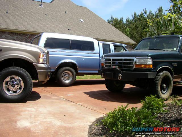 Green Ford F-Series truck in foreground, blue Ford Bronco with camper shell behind it, tan Ford F-Series truck to the left