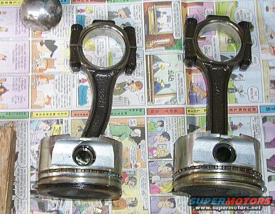 Two engine pistons with connecting rods on a newspaper background. A metal ball is in the upper left