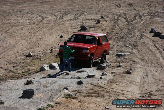 Red 1995 Ford Bronco on dirt road with person standing by hood
