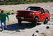 1995 Ford Bronco - A red Ford Bronco navigates a rocky, off-road terrain with a young man observing.