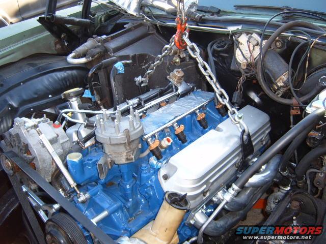 Engine with blue block and silver valve covers being lifted by a chain hoist