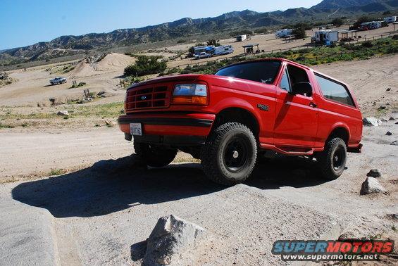 Red 1995 Ford Bronco on a dirt trail with mountains in the background