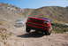 1995 Ford Bronco - A red 1995 Ford Bronco navigates a dusty trail in a hilly, arid landscape, with another SUV following behind.