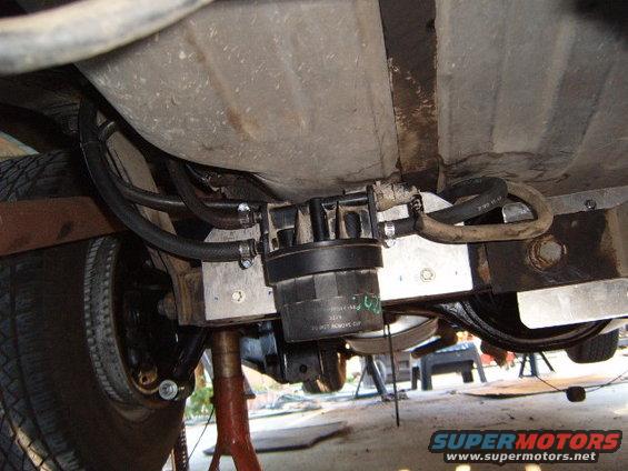 Underside view of a vehicle's fuel filter assembly, with hoses connected to a fuel tank