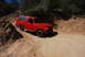 1995 Ford Bronco - A red SUV navigates a dusty, off-road trail under a clear blue sky.