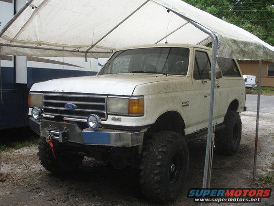White Ford Bronco with winch and aftermarket bumper under a tarp