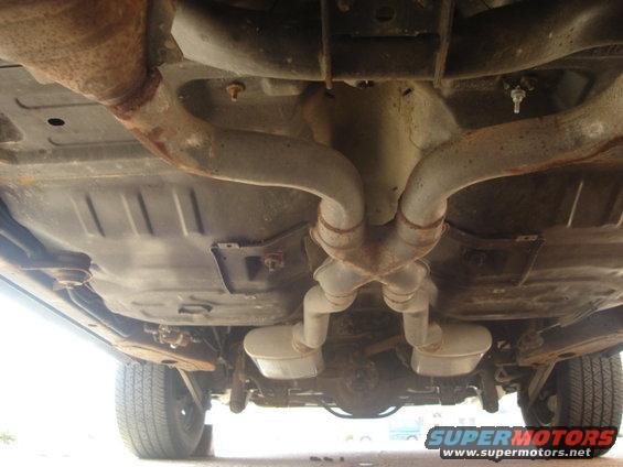 Underside of a vehicle showing rusty dual exhaust pipes and mufflers, with a rear differential visible