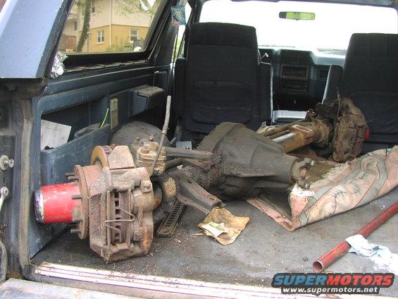 Interior view of a vehicle's cargo area filled with disassembled axles and brake parts