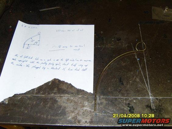 Paper with diagram and handwritten notes about a pulley system, next to a metal arc and string on a workbench