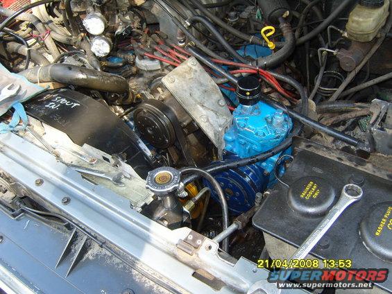 Engine bay with blue air conditioning compressor, hoses, and fan shroud. Text on shroud reads '3" STOUT IN.'