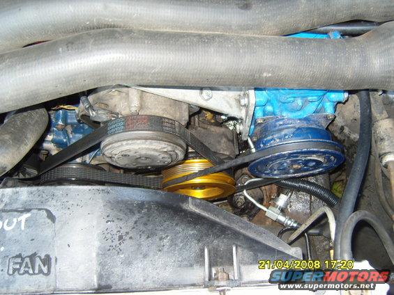 Engine bay view showing belts, pulleys, compressor, and fan shroud with text 'OUT FAN'
