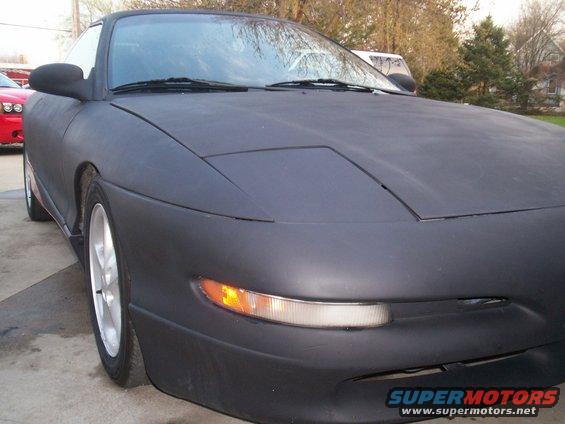 Matte black coupe front 3/4 view, red car in background