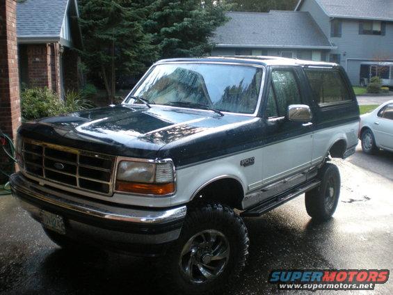 Two-tone dark green and white Ford Bronco with aftermarket wheels and tires, lifted suspension, parked on wet pavement