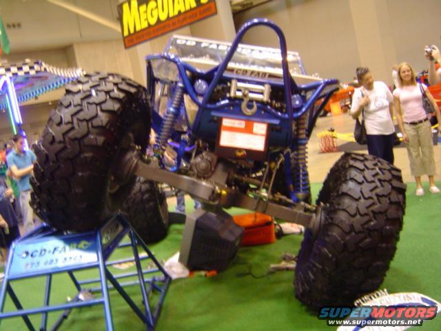 Custom blue off-road vehicle with large tires on display stands, front right tire visible
