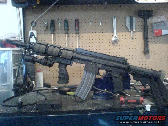 Assault rifle with flashlight and extended magazine on a workbench with tools in the background